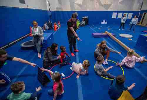 In a room full of blue pads, gv students and the childcare students play a game involving colorful hoops. 
